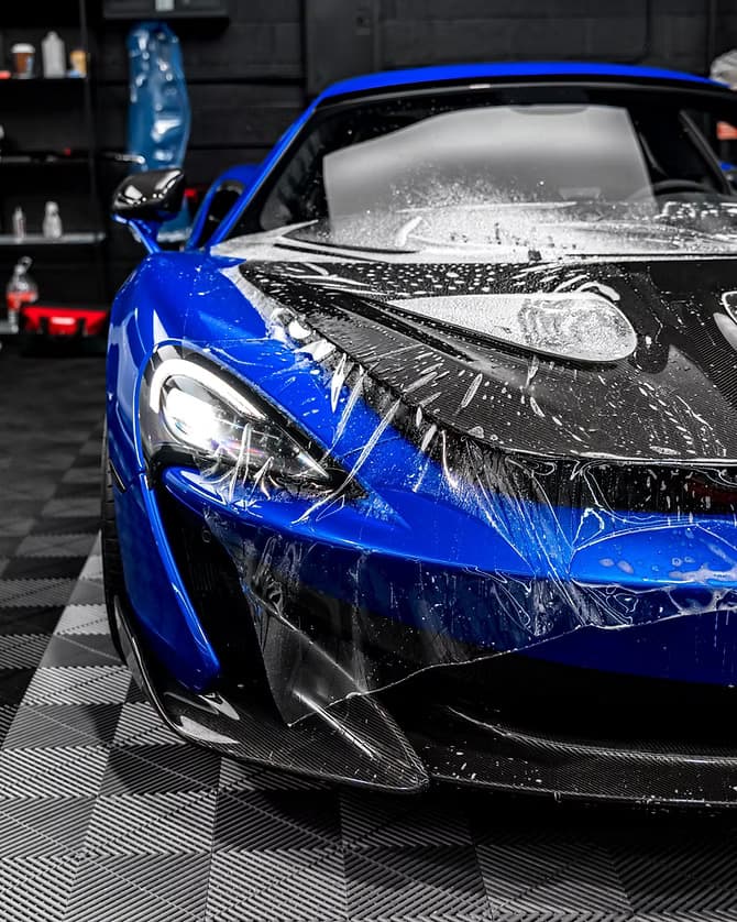 Technician precision-installing paint protection film on a vehicle's front bumper
